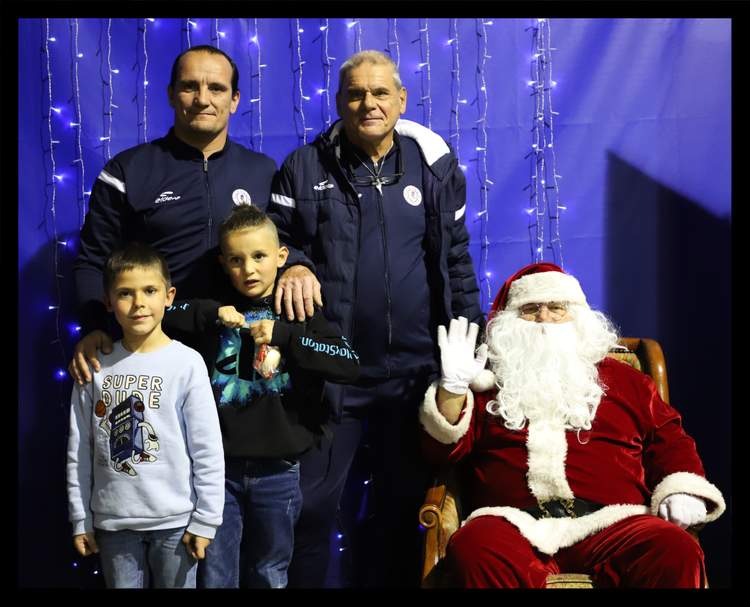 Des adultes et des enfants posent avec le Père Noël devant un fond bleu lumineux.