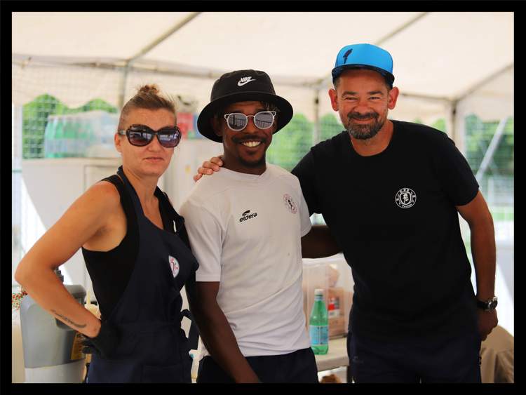 Trois personnes souriantes posent ensemble sous une tente lors d'un événement.