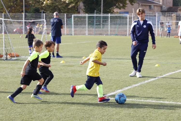 De jeunes footballeurs en tenue de sport s'entraînent sur un terrain en herbe synthétique sous le regard d'adultes.