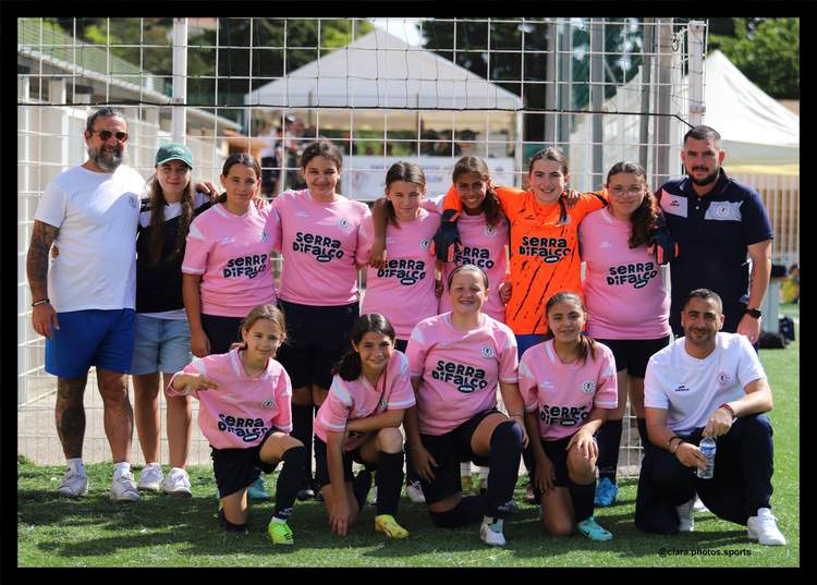 Une équipe de football féminine pose avec ses entraîneurs sur un terrain de sport.