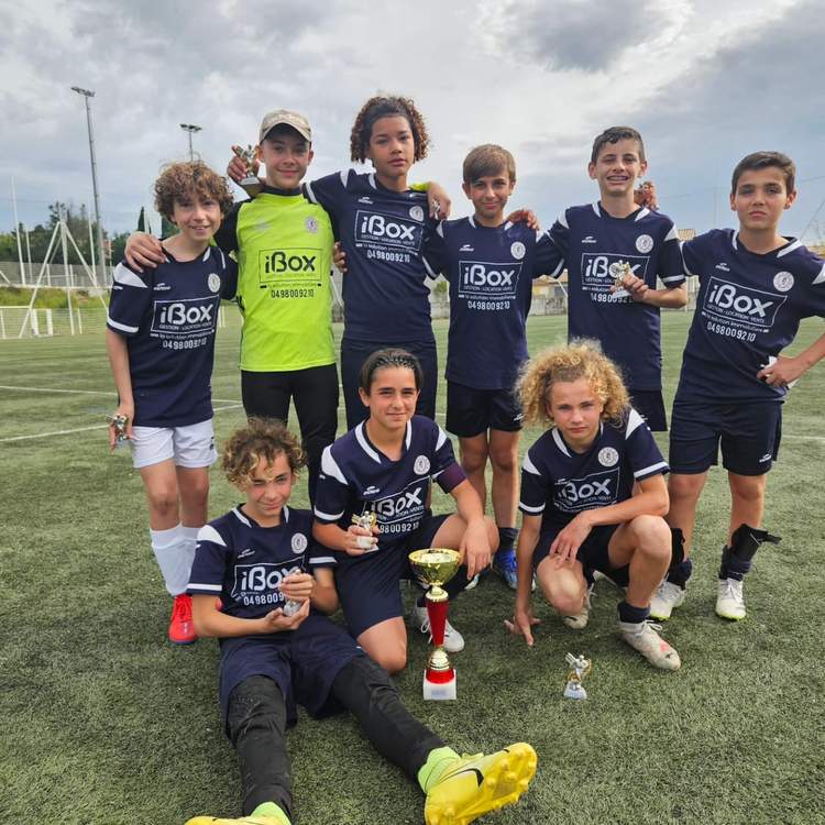 Une équipe de jeunes footballeurs pose fièrement avec leurs trophées sur un terrain de football.