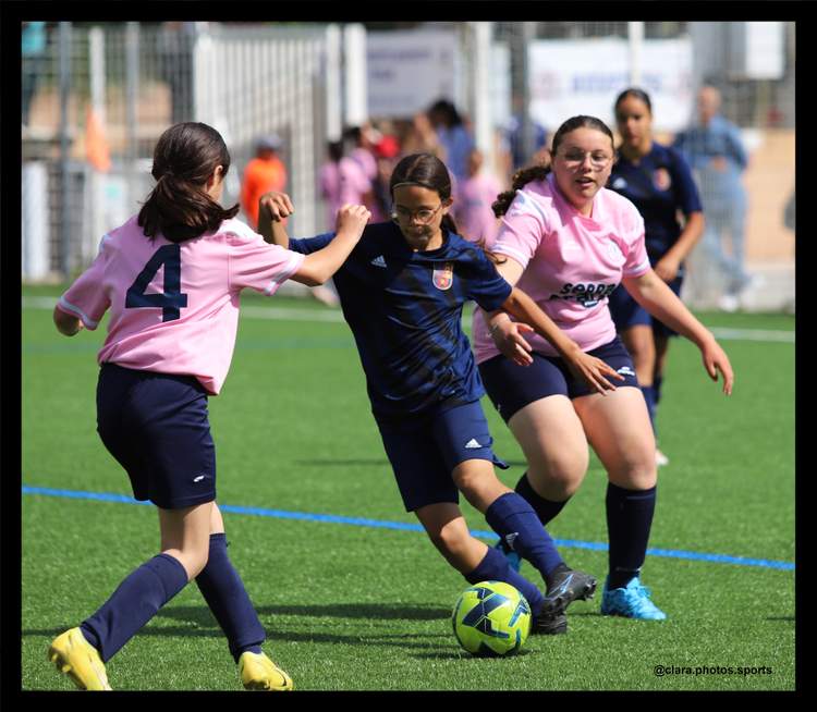 Trois jeunes joueuses de football féminin en pleine action sur un terrain en gazon synthétique, avec le ballon au centre.