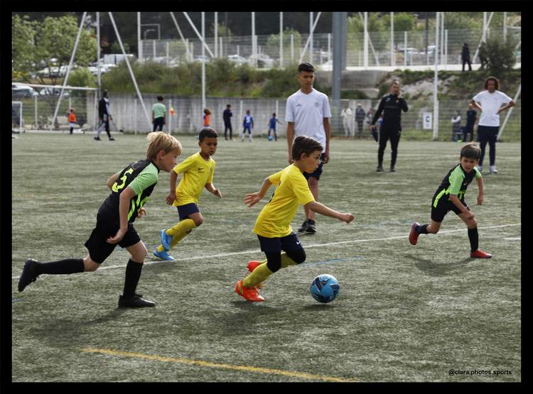 Des jeunes joueurs de football en pleine action sur le terrain, avec un ballon bleu au premier plan.