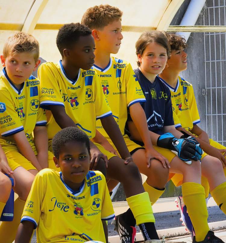 Des jeunes footballeurs en maillots jaunes et bleus sont assis sur un banc, certains regardant l'objectif.