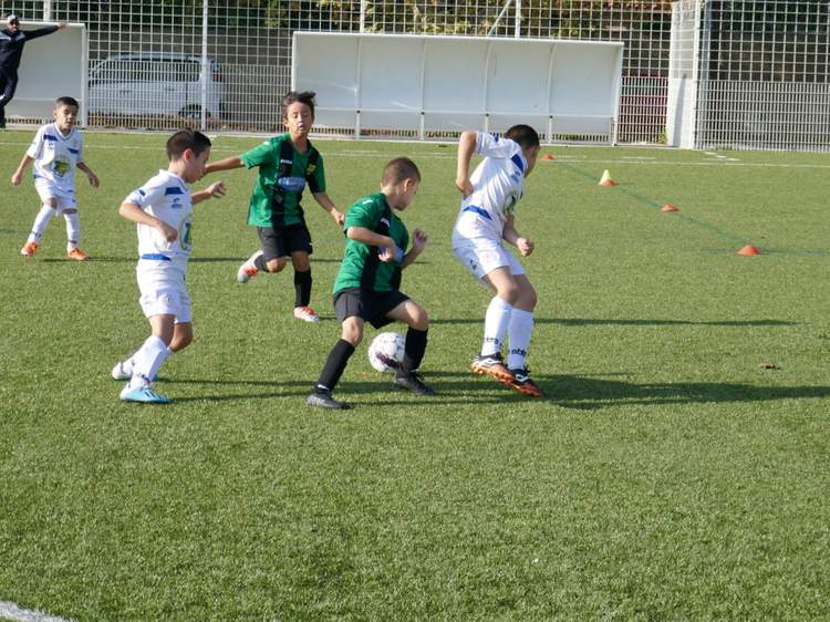 Des jeunes joueurs de football en maillots verts et blancs s'affrontent sur un terrain synthétique en plein jour.