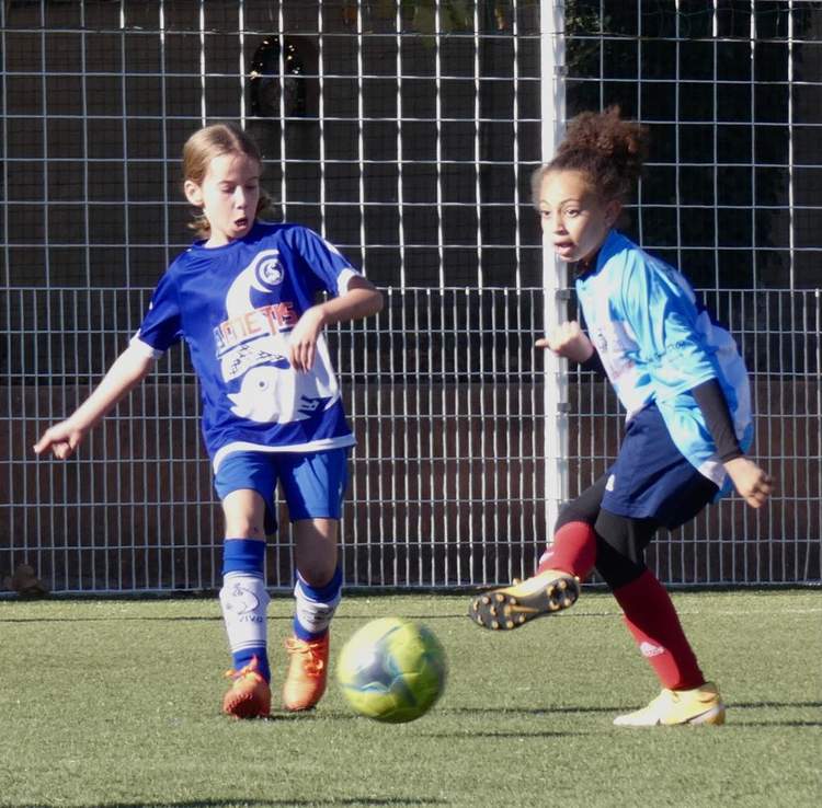 Deux jeunes joueuses de football en pleine action sur un terrain synthétique, l'une s'apprêtant à frapper le ballon.