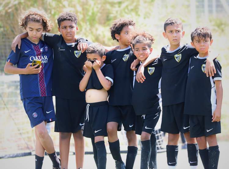 Un groupe de jeunes footballeurs pose ensemble sur le terrain, certains se tenant par les épaules.