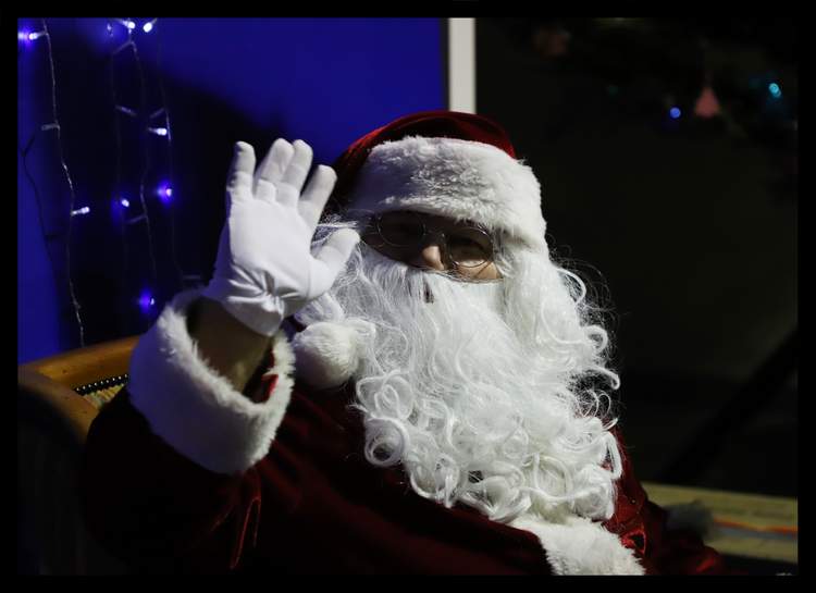 Un Père Noël avec une longue barbe blanche et des lunettes salue de la main.