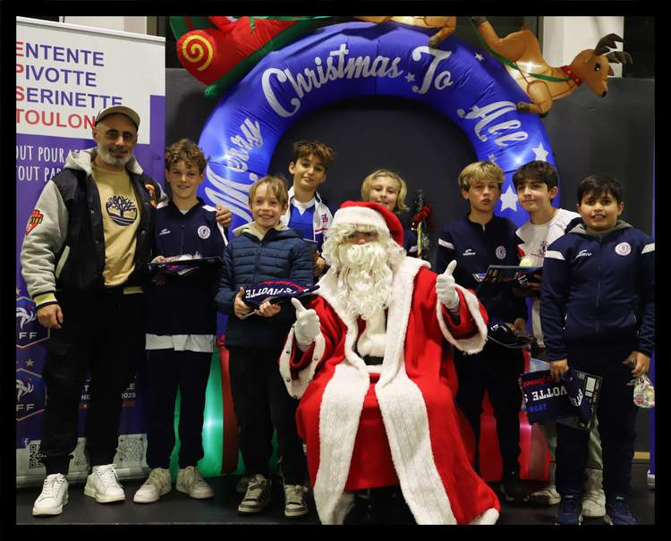Un groupe d'enfants et d'adultes posent avec le Père Noël devant une arche gonflable de Noël.