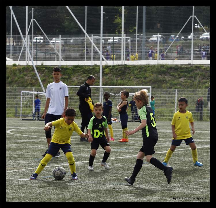 Des jeunes joueurs de football s'entraînent sur un terrain en herbe synthétique, sous la supervision d'adultes.