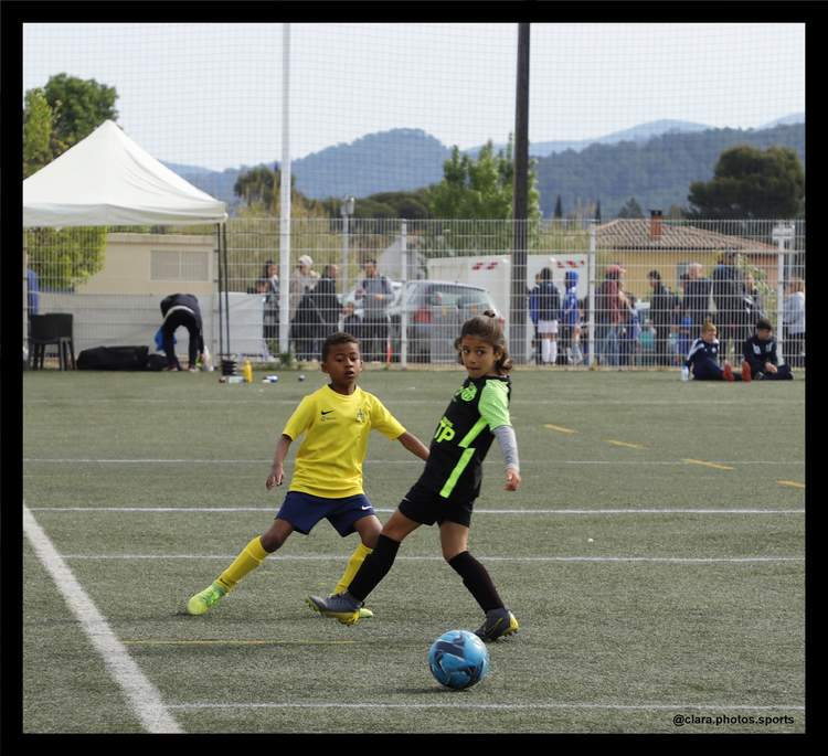Deux jeunes joueurs de football, un garçon et une fille, en pleine action sur le terrain avec un ballon.