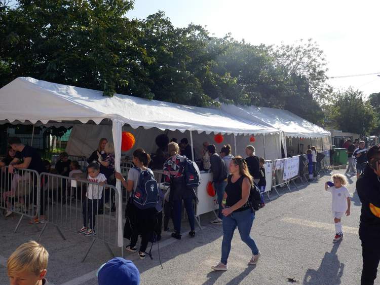 Une foule de personnes se rassemble sous des tentes blanches lors d'un événement en plein air.