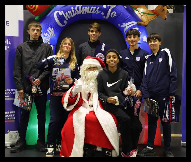 Des jeunes joueurs de football posent avec le Père Noël devant une arche de Noël gonflable.