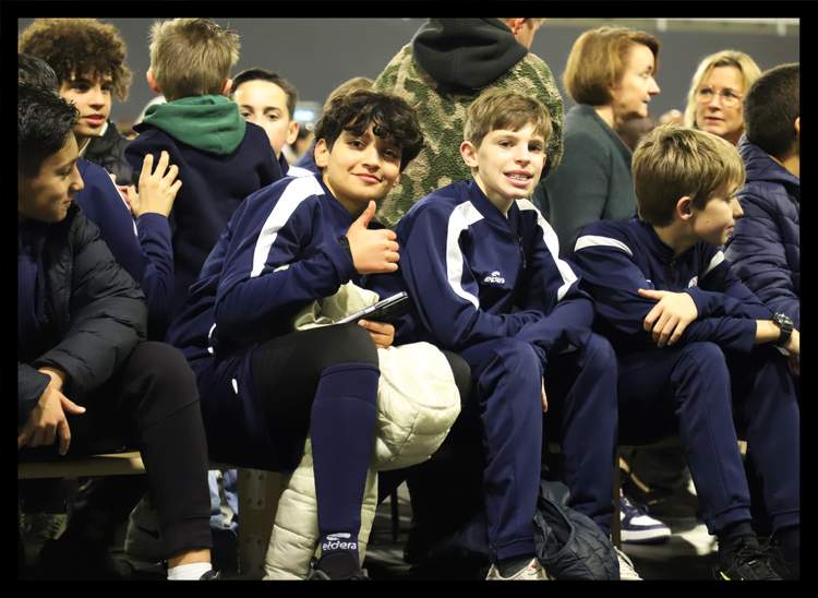 Des jeunes joueurs de football sont assis et regardent un événement, l'un d'eux fait un pouce levé.