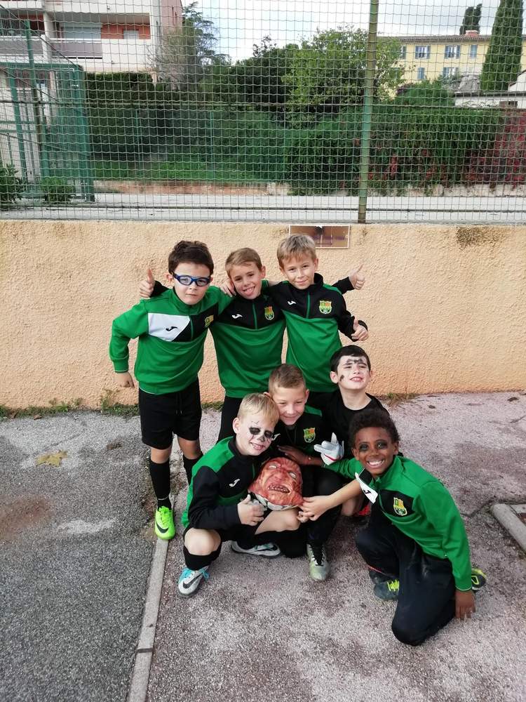 Un groupe de jeunes footballeurs souriants en maillots verts posent ensemble, certains avec du maquillage ou un masque.