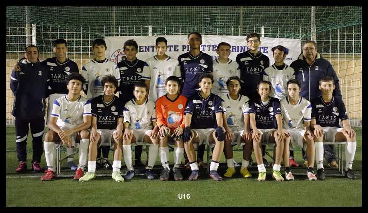 Une équipe de football junior pose pour une photo de groupe sur un terrain de sport en soirée.