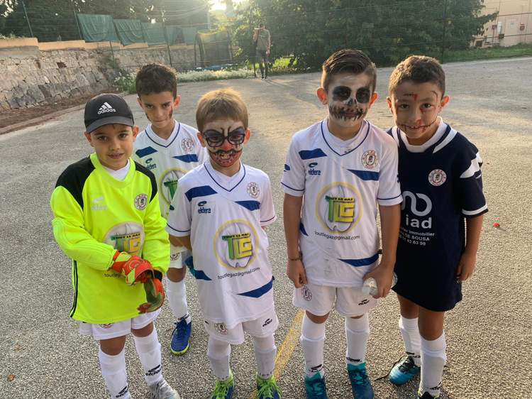 Cinq jeunes footballeurs posent avec des maquillages de fête sur le terrain.