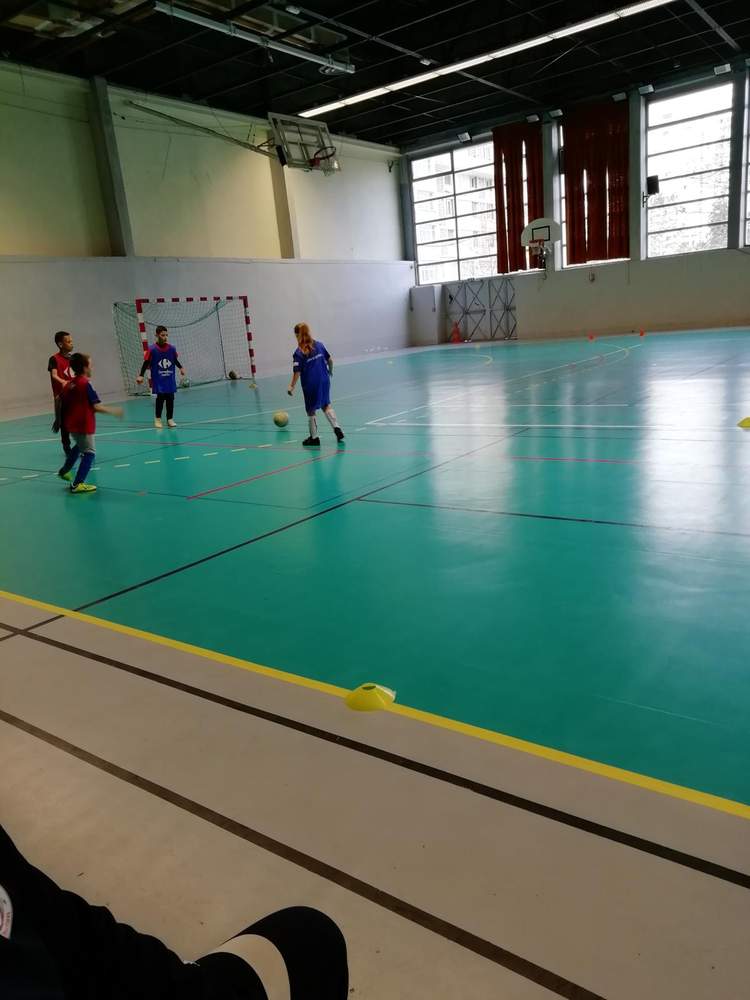 Des enfants jouent au football en salle sur un terrain vert avec un but.