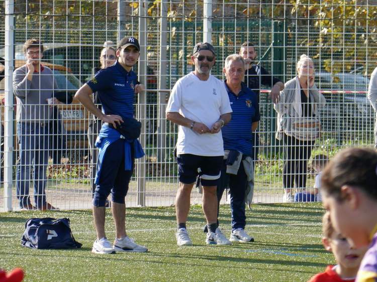 Des adultes et des enfants observent un événement sportif derrière une clôture sur un terrain de football.