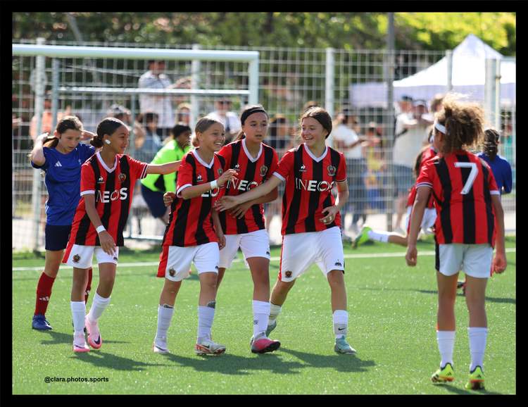 Des jeunes joueuses de football en maillot rayé rouge et noir se regroupent sur le terrain pendant un match.