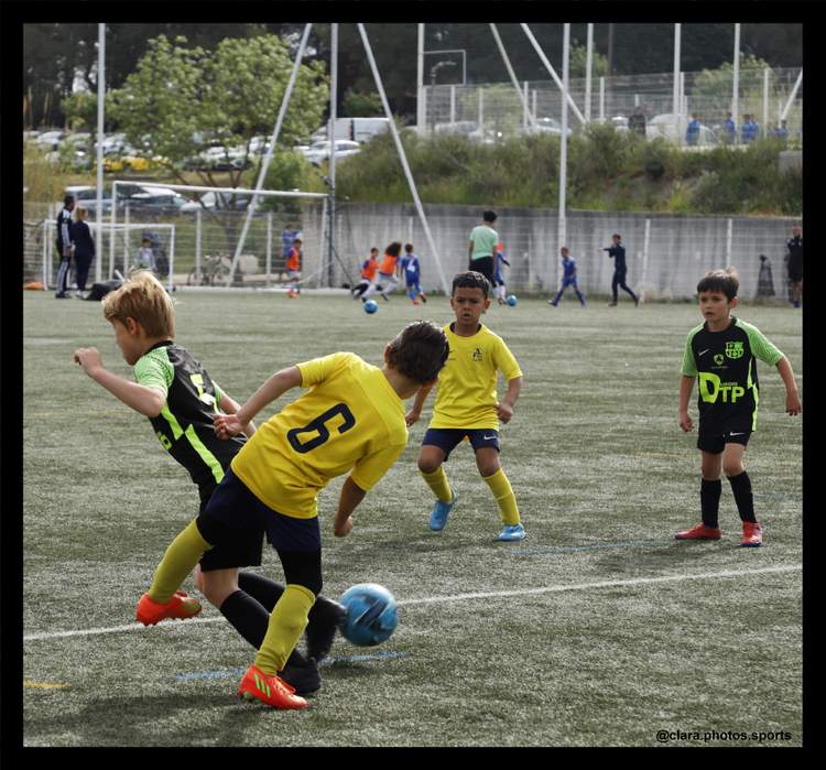 Des jeunes joueurs de football en pleine action sur un terrain en herbe, avec plusieurs enfants en arrière-plan.