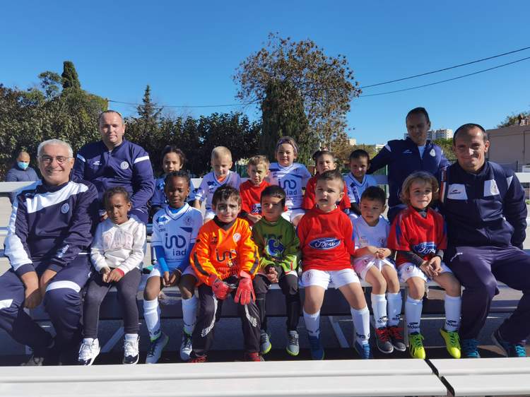 Une équipe de jeunes footballeurs et leurs entraîneurs posent pour une photo de groupe en extérieur sous un ciel bleu.