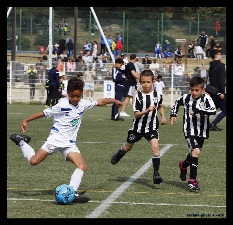 Trois jeunes joueurs de football en pleine action sur le terrain, avec un public en arrière-plan.