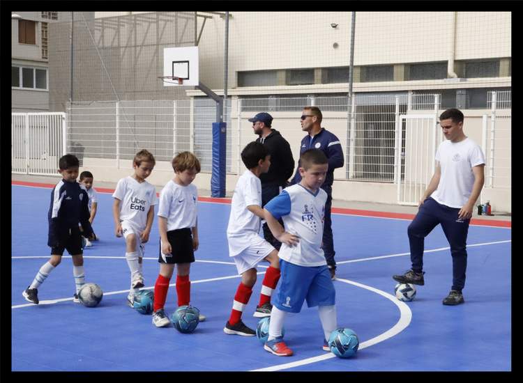 Des jeunes joueurs de football s'entraînent avec des ballons sur un terrain bleu, encadrés par des adultes.