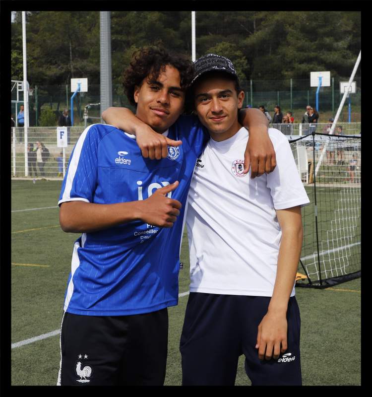 Deux jeunes joueurs de football posent bras dessus bras dessous sur un terrain de sport.