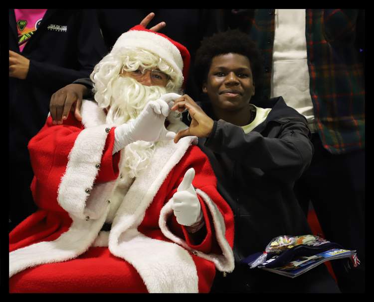 Un jeune homme souriant pose avec une personne déguisée en Père Noël, faisant un signe de cœur avec les mains.