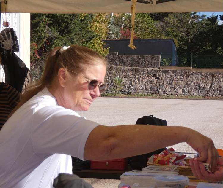 Une femme aux lunettes de soleil tend la main pour prendre de l'argent à un stand extérieur.