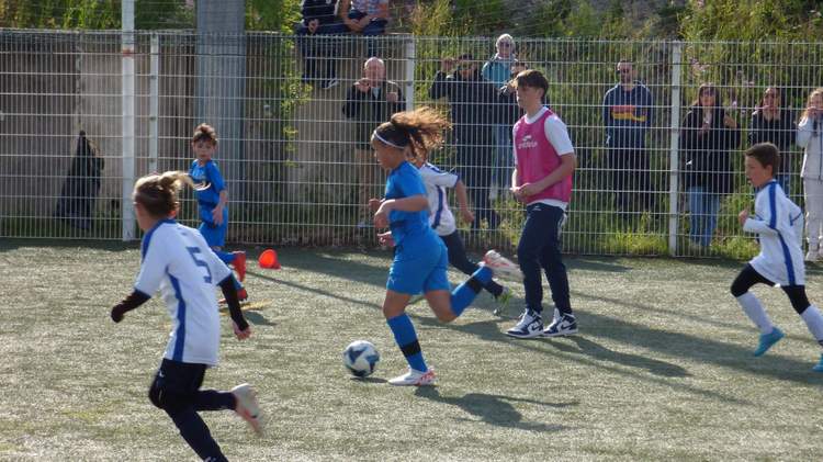 Des jeunes joueurs de football en pleine action sur un terrain synthétique, avec des spectateurs en arrière-plan.