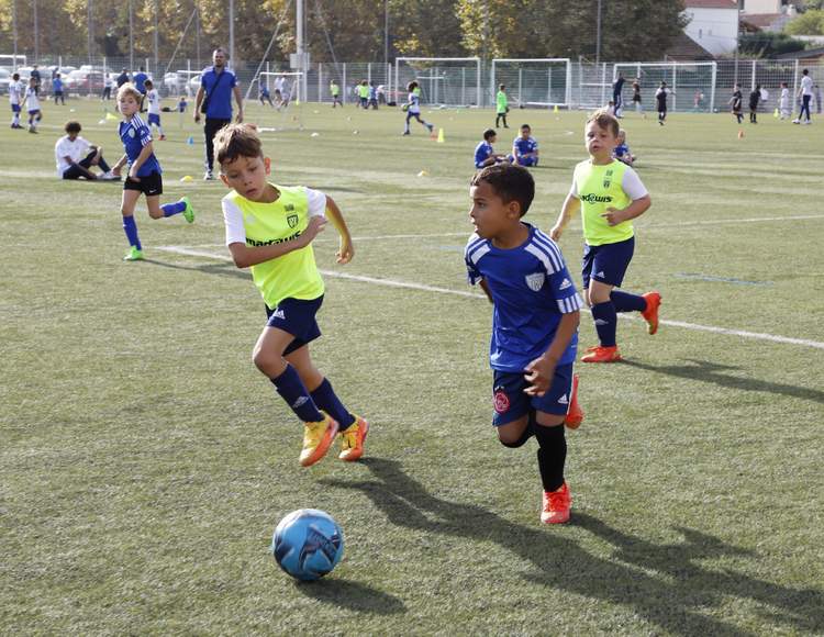 Des jeunes joueurs de football en pleine action sur un terrain ensoleillé, avec un ballon au premier plan.