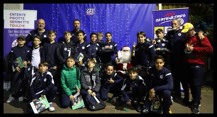 Un groupe de jeunes footballeurs et d'adultes, dont un Père Noël, posent ensemble devant une toile de fond bleue décorée.