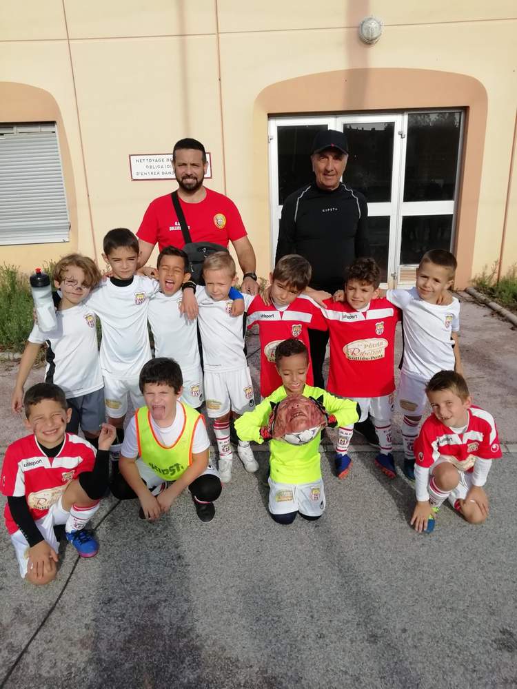 Une équipe de jeunes footballeurs pose avec leurs entraîneurs devant un bâtiment.