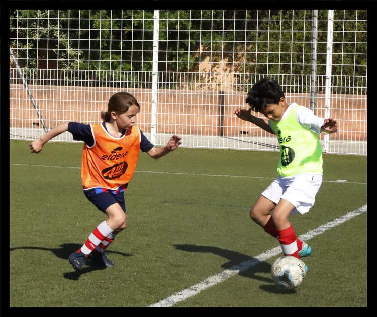 Deux jeunes joueurs de football en chasubles s'affrontent pour le ballon sur un terrain ensoleillé.