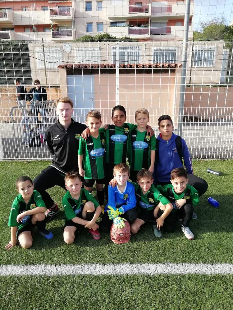 Une équipe de jeunes footballeurs pose avec leur entraîneur sur un terrain en gazon synthétique.