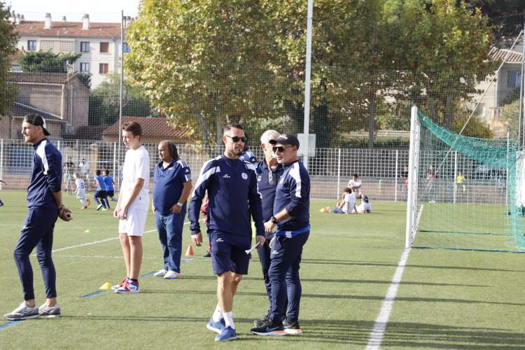Des adultes et des enfants sur un terrain de football synthétique, avec des entraîneurs en tenue de sport.