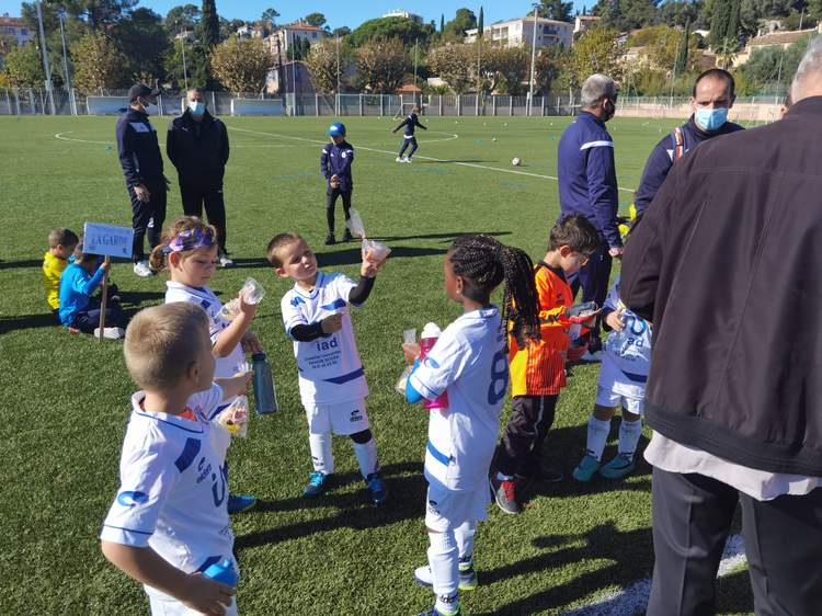 Des jeunes joueurs de football boivent et se reposent sur le terrain après l'effort, encadrés par des adultes.