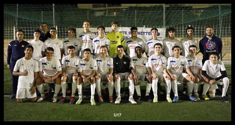 Une équipe de football junior pose pour une photo de groupe sur un terrain en gazon synthétique, avec des adultes encadrants.