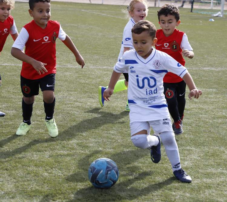 De jeunes footballeurs en maillots de différentes couleurs jouent au football sur un terrain en gazon synthétique.