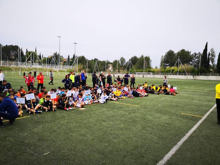 De nombreux jeunes joueurs de football sont assis sur le terrain, entourés d'adultes, lors d'un événement sportif.