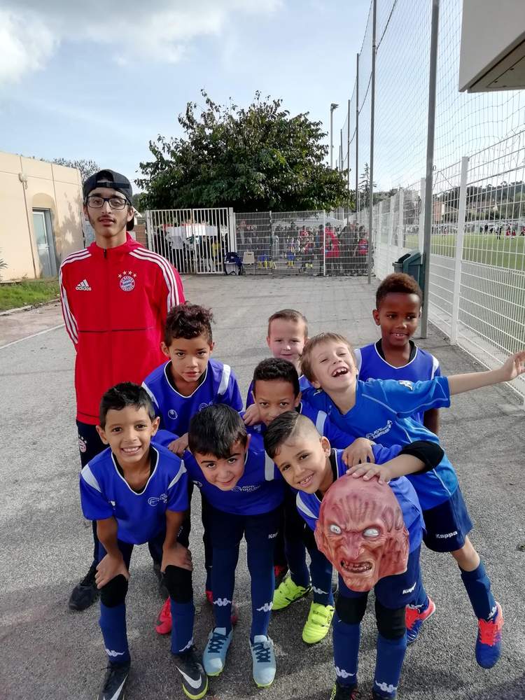 Un groupe de jeunes footballeurs et leur entraîneur posent pour une photo d'équipe sur un terrain de sport.