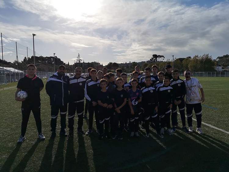 Une équipe de jeunes footballeurs et leurs entraîneurs posent sur un terrain de sport sous un ciel nuageux.