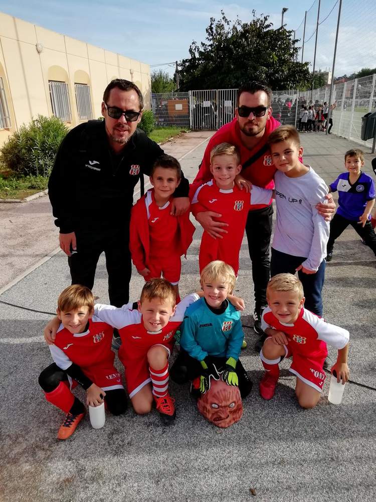 Une équipe de jeunes footballeurs pose avec leurs entraîneurs sur un terrain extérieur.