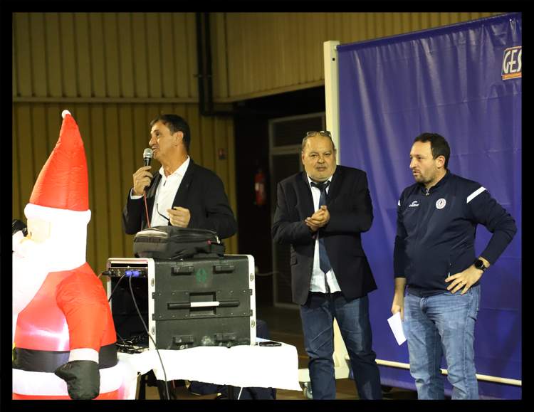 Trois hommes, dont un au micro, lors d'un événement festif avec une décoration de Noël.