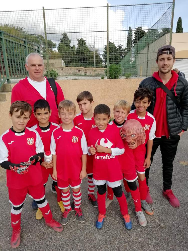 Une équipe de jeunes footballeurs en maillots rouges posent avec leurs entraîneurs sur un terrain de sport.