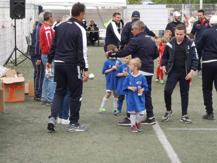 Des adultes et des enfants en tenue de sport se rassemblent sur un terrain de football, certains enfants tenant des trophées.