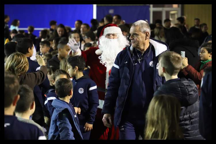Le Père Noël et un entraîneur au milieu d'un groupe d'enfants lors d'un événement festif.