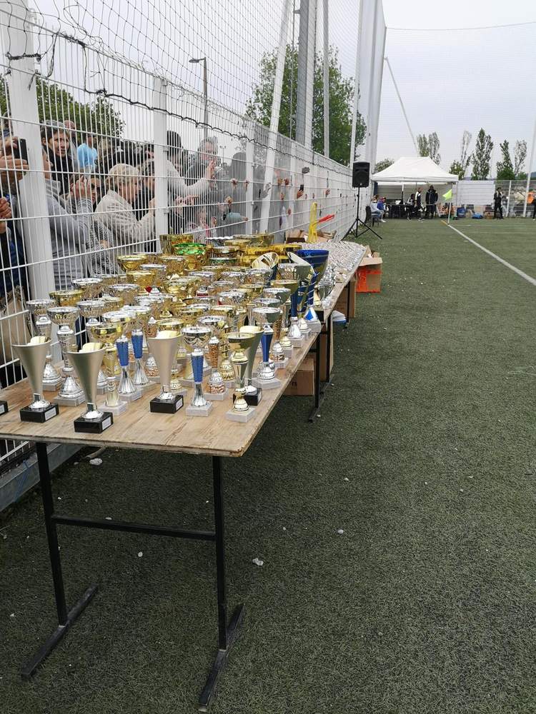 Une table remplie de trophées devant une foule de spectateurs derrière une clôture, sur un terrain de football.
